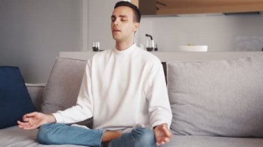 Kafkasyalı genç bir adamın, sabahın erken saatlerinde kanepede otururken lotus pozisyonunda meditasyon yaparken yakın plan çekimleri.