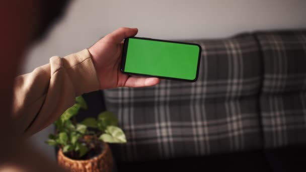 Handheld Camera: standpunt van de mens in de moderne kamer Zittend op een stoel met behulp van telefoon met groene Mock-up scherm Chroma Key Surfen op internet Inhoud video 's bekijken — Stockvideo