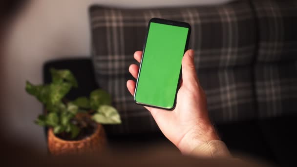 Портативна камера: точка зору людини в сучасній кімнаті сидить на стільці, використовуючи телефон із зеленим макетним екраном Chroma Key Surfing Internet Watching Content Videos — стокове відео