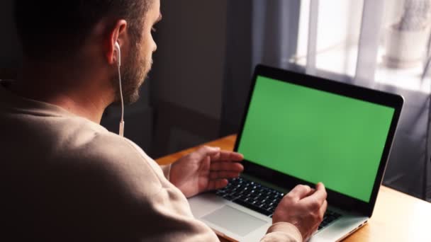Νεαρός καυκάσιος άνδρας στο γραφείο του σπιτιού κάθεται τραπέζι επικοινωνεί μιλάμε με πράσινη οθόνη φορητό υπολογιστή. Αντρική ομιλία από online απομακρυσμένο συνέδριο web cam video call — Αρχείο Βίντεο