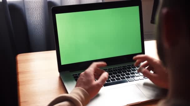 办公室里年轻的高加索人坐在桌子上与绿色屏幕笔记本电脑交流。男性通过在线远程会议摄像头视频通话 — 图库视频影像
