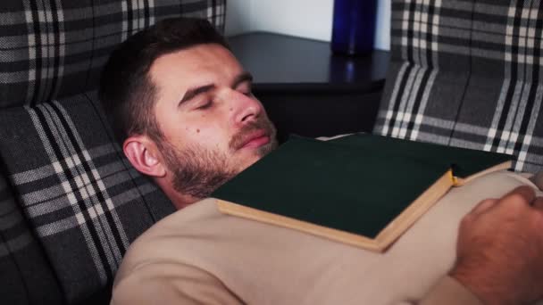 Надмірно зайнятий, втомлений молодий кавказький чоловік вдома спить під книгою . — стокове відео