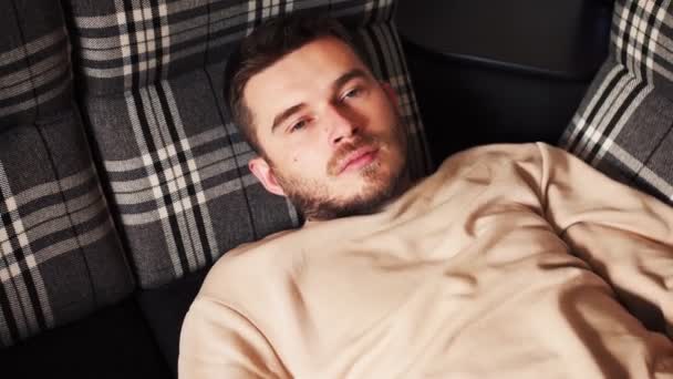 Junger Kaukasier entspannt sich auf der Couch mit den Händen hinter dem Kopf — Stockvideo
