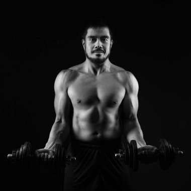Koyu arka plan üzerinde dumbbells ile güçlü genç adam