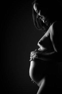 Çıplak hamile kadın karnına dokunuyor. Yan görünüm, siyah ve beyaz göbek kapatın. Siyah üzerinde izole.
