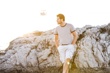 Genç adam sahilde oturuyor. 