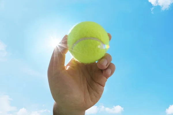 green tennis ball in hand against sky