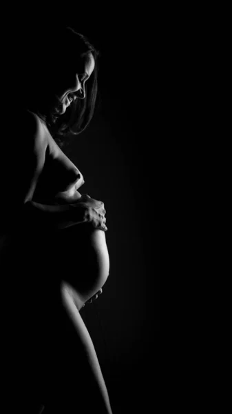 Stock image Nude pregnant woman touching her belly. Side view, black and white belly close up. Isolated on black.