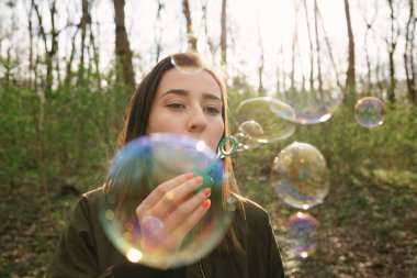 Genç bir kadın ormanda sabun köpüğü üflüyor. Özgürlük, yaşam tarzı ve ağ kurma kavramı. Renkli analog film görünümü.