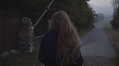 Bir kadın yolda yürür ve gökyüzüne köy ve bariyer arka planı bakar.