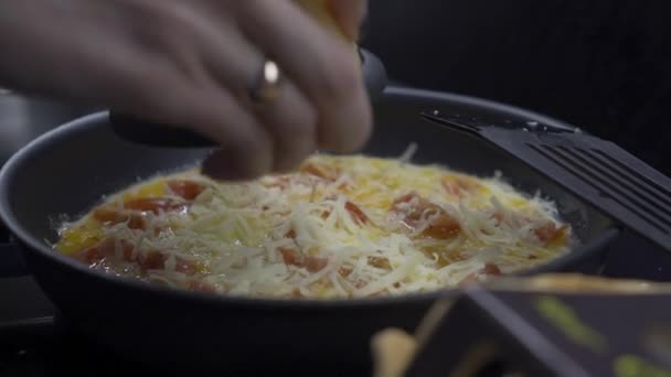 Femme frotte du fromage sur des œufs brouillés dans une poêle — Video