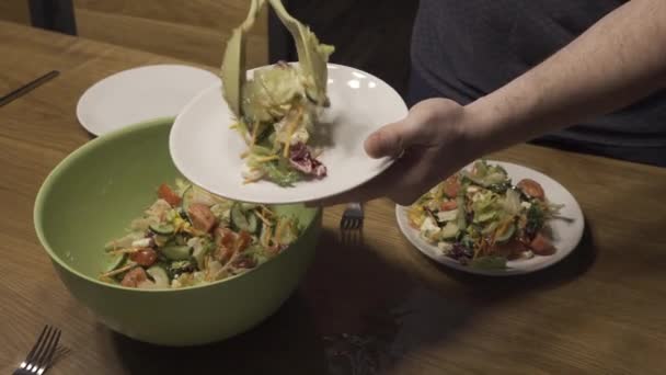 Člověk klade salát v talíř na pozadí desky se salátem — Stock video