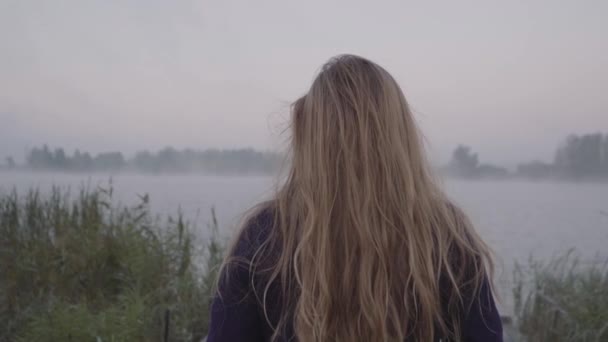 Młoda kobieta idzie w kierunku jeziora i jej długie włosy kołysze się na wietrze — Wideo stockowe