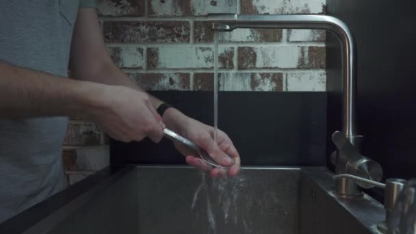 Ένας άνθρωπος πλένει ένα κουτάλι με σφουγγάρι καθαρισμού στην κουζίνα — Αρχείο Βίντεο