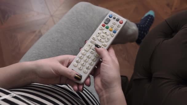 Uma mulher pega no controle remoto e pressiona os botões, e depois o traz de volta — Vídeo de Stock