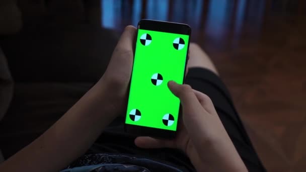 Guapo en casa usando smartphone. Primer plano de una mano adolescente sosteniendo un teléfono móvil con una pantalla verde vertical — Vídeos de Stock