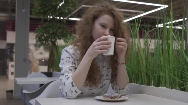 Joven hermosa mujer pelirroja se sienta en un café y bebe café con malvaviscos — Vídeo de stock