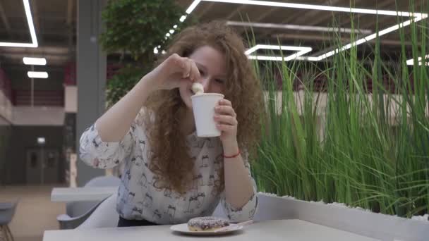 Giovane bella donna dai capelli rossi si siede in un caffè e mangia marshmallows da caffè — Video Stock