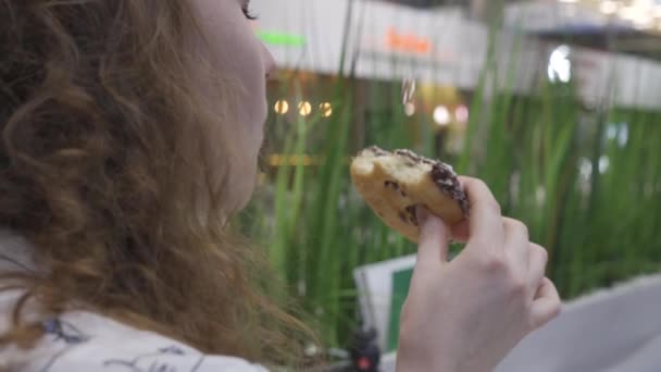 Retrato de uma bela menina feliz com o cabelo vermelho comendo um donut, olhando para a câmera — Vídeo de Stock
