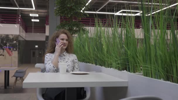 Bella giovane donna seduta a un tavolo in un caffè, parlando al telefono — Video Stock