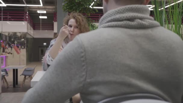 Young beautiful woman with red curly hair eats Caesar salad in a cafe and sits opposite a man — Stock Video