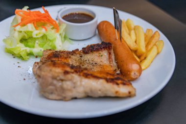 Patates ve salatalar ile beyaz bir tabak üzerinde biftek.