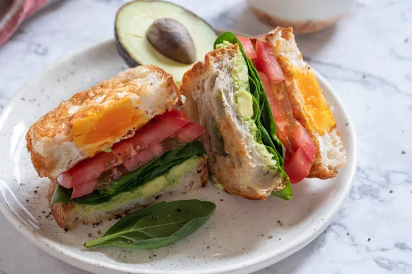 Egg in a hole sandwich with avocado, spinach and tomato