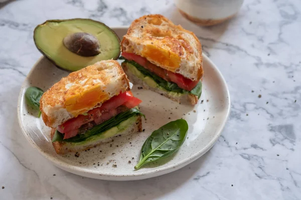 Egg in a hole sandwich with avocado, spinach and tomato