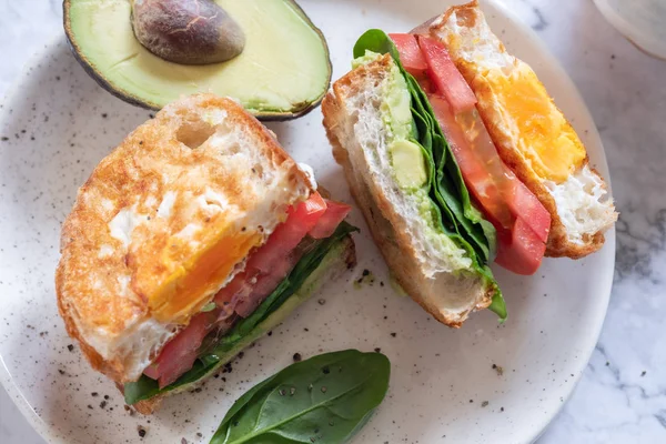 Egg in a hole sandwich with avocado, spinach and tomato