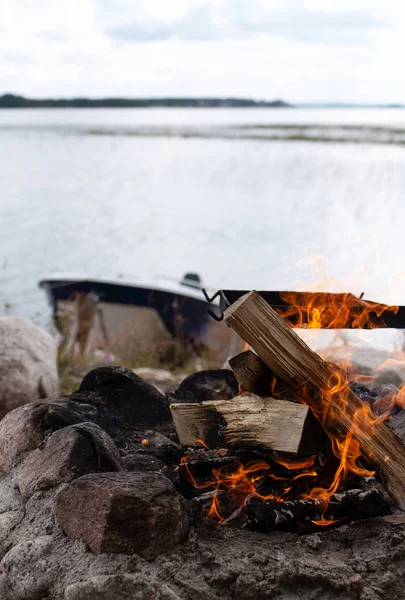 A crackling campfire next to a boat and a lake - nordic summer view