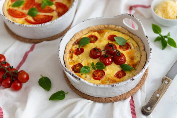 Tomato pies with basil leaves, chicken ans cheese on white tablecloth. Homemade french quiche with cherry tomatoes