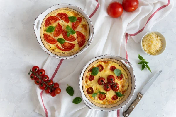 Tomato pies with basil leaves, chicken ans cheese on white tablecloth. Homemade french quiche with cherry tomatoes