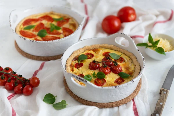 Tomato pies with basil leaves, chicken ans cheese on white tablecloth. Homemade french quiche with cherry tomatoes