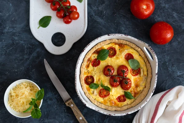 Tomato pies with basil leaves, chicken ans cheese with ingredients on dark background. Homemade french quiche.