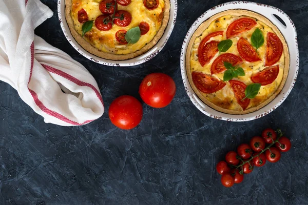 Tomato pies with basil leaves, chicken ans cheese with ingredients on dark background. Homemade french quiche. Top view