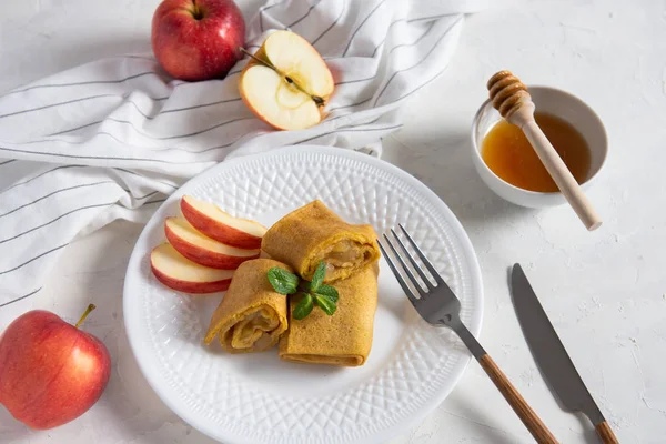 Crepes with apple sauce, cinnamon and honey on white background