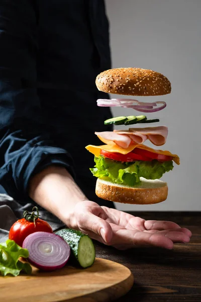 Levitating burger over the man's hand. Flying burger's ingredients in the air.