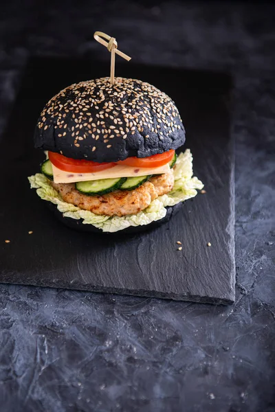 Fast food concept. Black burger with delicious meat, tomatoes, cucumbers, cheese and lettuce on a black background. Side view. copy space. Restaurant, menu,