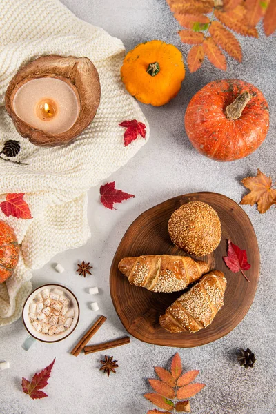 Cozy autumn morning breakfast flat lay. Cup of hot cocoa with marshmallows, croissants, pumpkins leaves and candle. Fall, Thanksgiving, bakery concept.