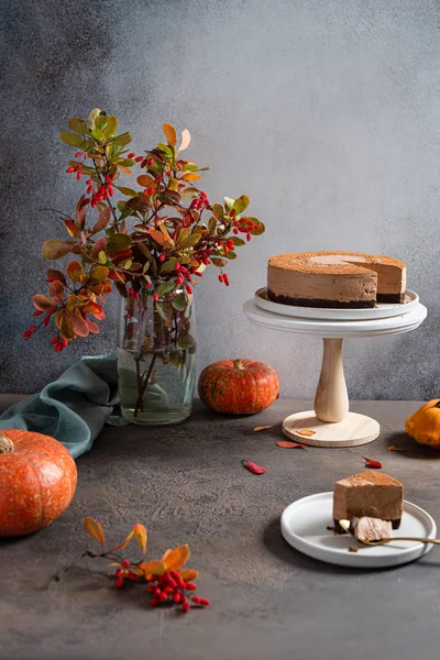 Cozy autumn composition. Chocolate mousse cake on the stand surrounded by autumn leaves and pumpkins on a gray table. Greeting card, cafe, confectionery, bakery, Thanksgiving concept, copy space