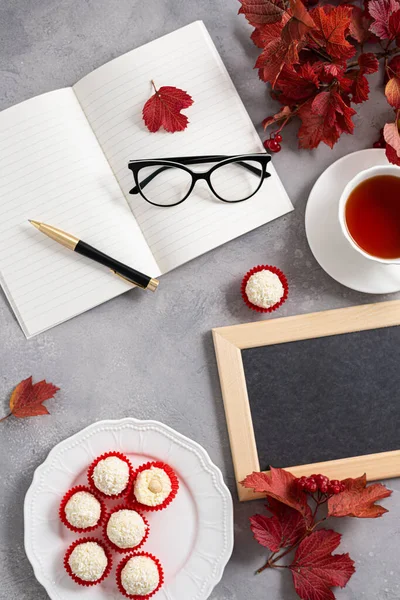 Teacher\'s day greeting card concept. Red autumn leaves, notebook, glasses, pen, tea, candies and black empty chalkboard with copy space on gray background.