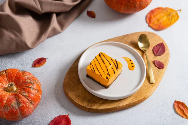 Homemade pumpkin cheesecake pie recipe with cinnamon on white table with pumpkins and autumn leaves on the background. Halloween party traditional dessert. Thanksgiving, menu