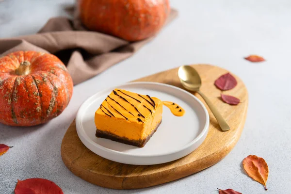 Homemade pumpkin cheesecake pie recipe with cinnamon on white table with pumpkins and autumn leaves on the background. Halloween party traditional dessert. Thanksgiving, menu