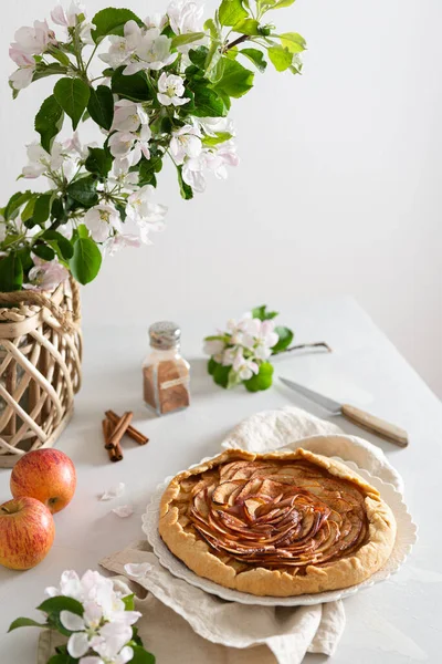 Homemade Galette Pie with Apples and cinnamon on white table with blossom branches. Side view, copy space for text. Bakery banner. Cookbook recipe