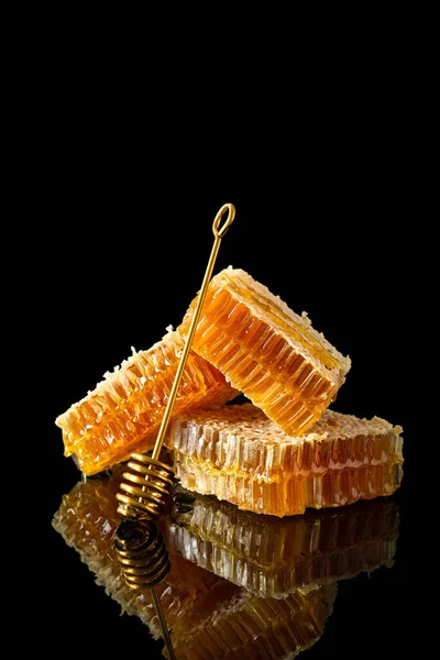 Honeycomb with natural honey and golden dipper on black background with reflection. Side view, close up, vertical. Natural, organic food. Beekeeping advertisement, banner, store
