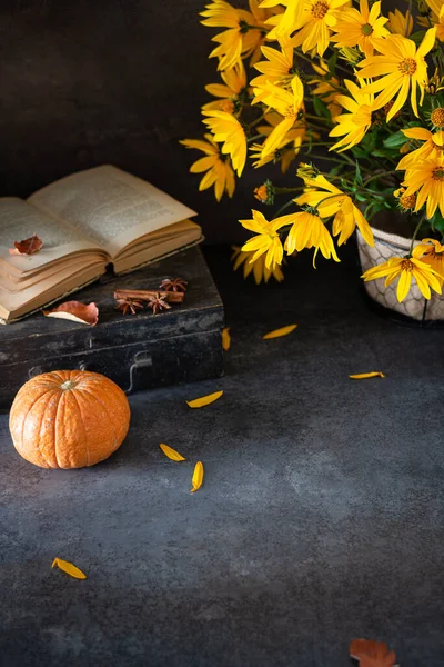 Cozy Autumn composition. Hygge. Open book, autumn leaves, pumpkins and yellow flowers on dark vintage background. Fall mood, autumn vibes. Copy space for text, product place