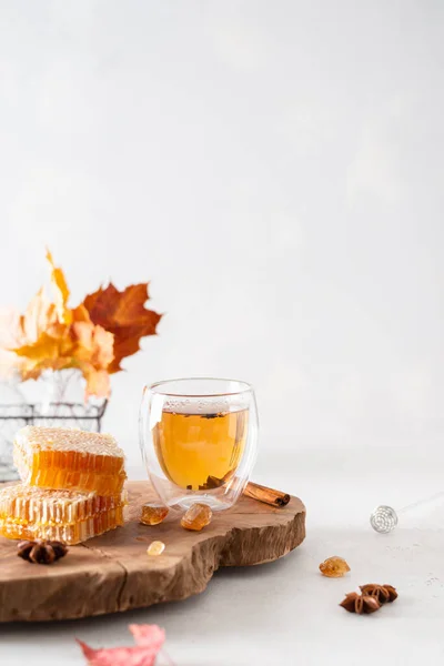 Cozy autumn concept, hygge. Cup of hot black tea, teapot, honey combs, autumn leaves on wooden tray on white background. Strengthening immunity. Side view, copy space for text. Autumn tea party