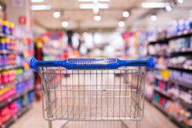 Süpermarket koridorundaki alışveriş arabası görüntüsü. Ürün rafları soyut bulanık arka plan.