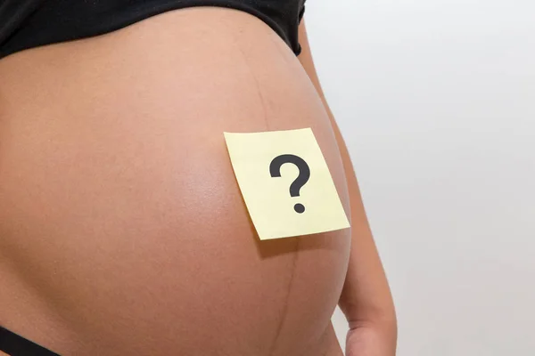 Belly of a young pregnant woman with a white sticker and a question on it (boy or girl concept)