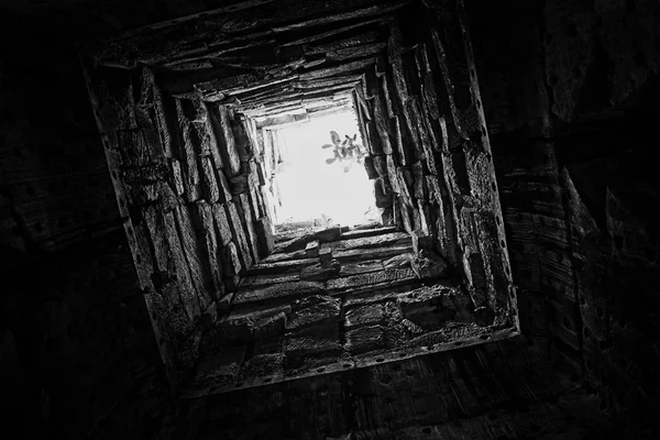 Derin kuyu, duvarları taşla kaplı. Alt görünüm. Tünelin sonundaki ışık. Yolun sonundaki ışık. Arka plan.